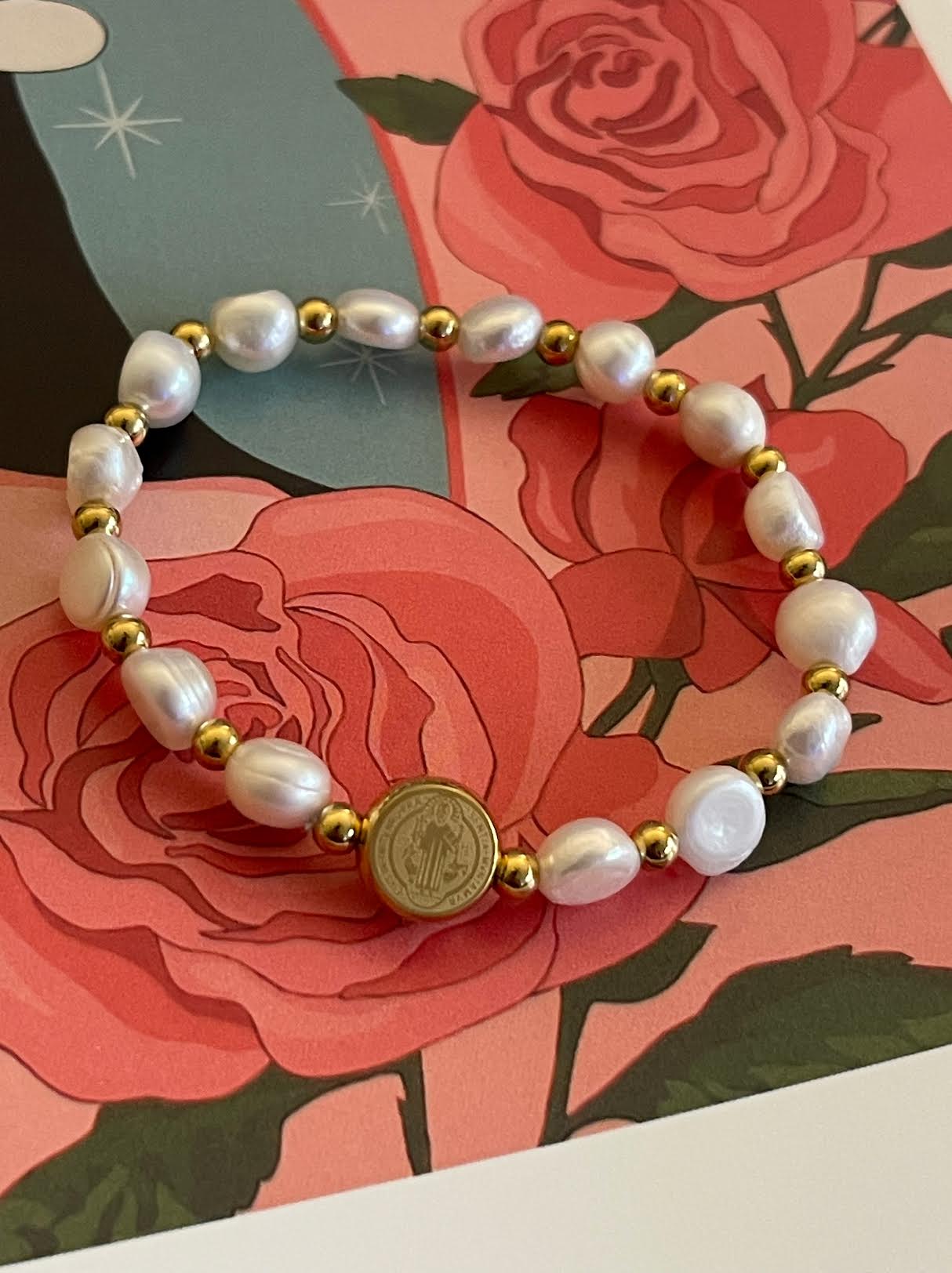 Pulsera Hippie Chic elasticada de elegantes piedras naturales blancas y imagen de San Benito por un lado y cruz por el otro en acero inoxidable dorado.