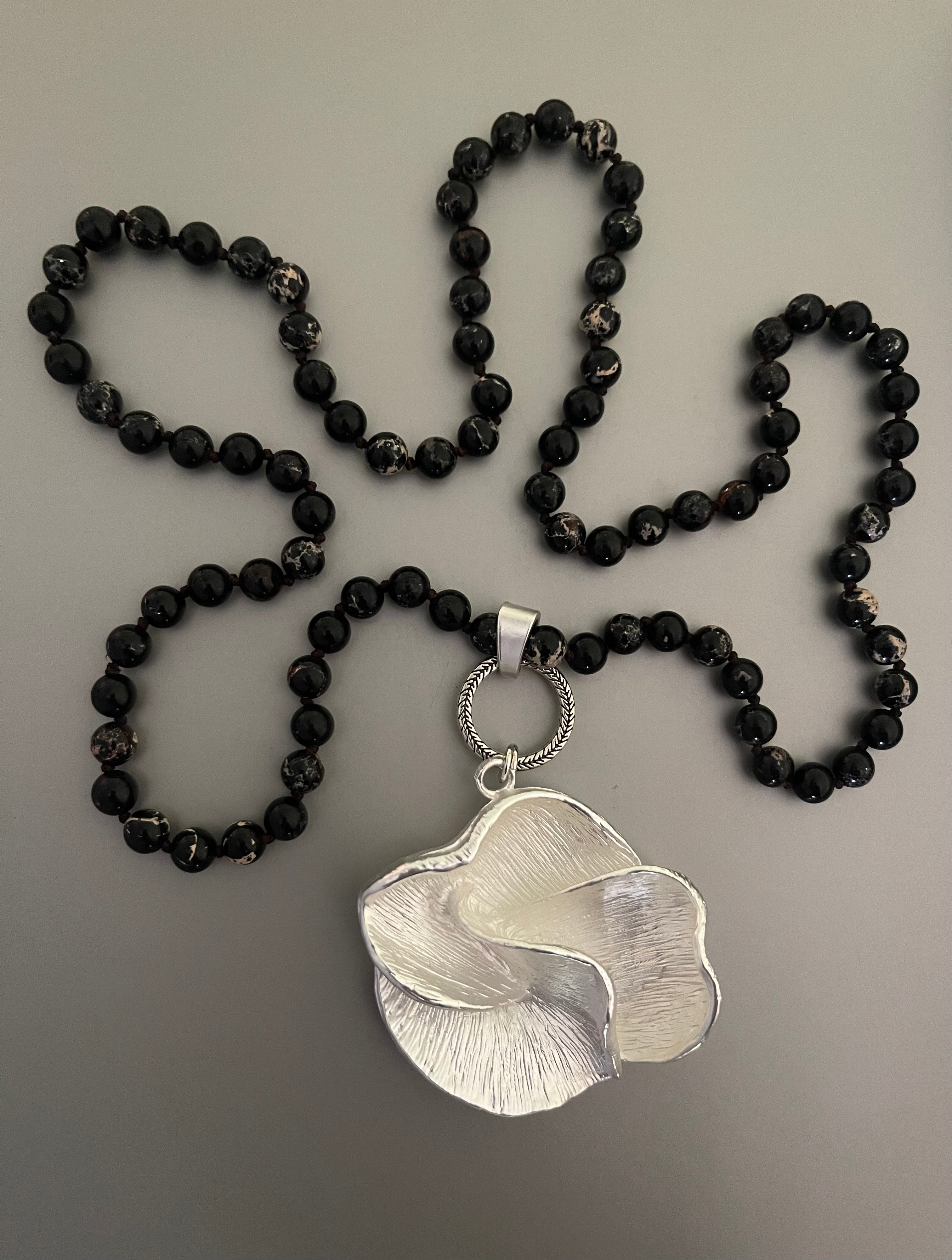 Collar Hippie Chic largo con precioso colgante de flor plateado opaco y piedras naturales anudadas negras con leves vetas blancas.