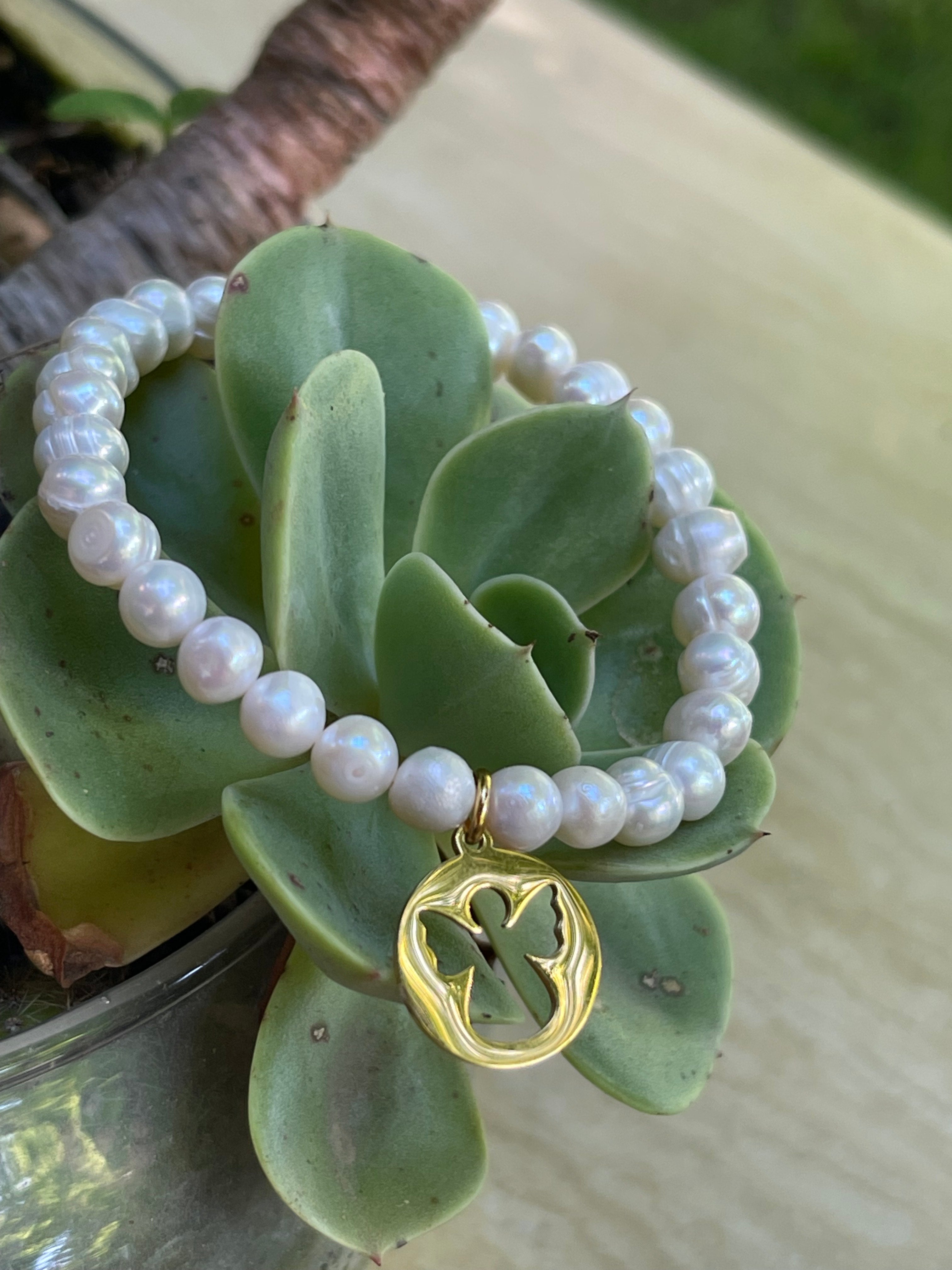 Pulsera Hippie Chic elasticada de finas perlas naturales blancas y colgante de Angelito en acero inoxidable dorado.