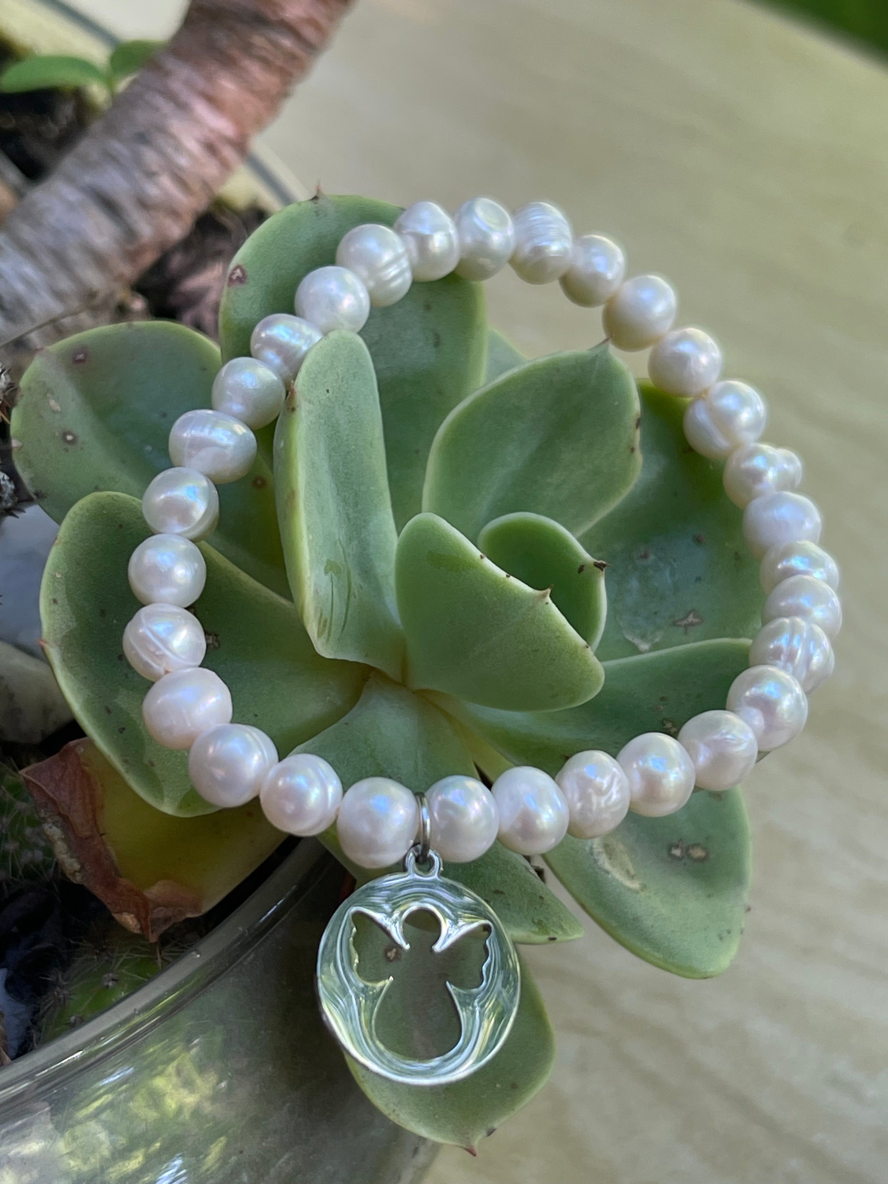 Pulsera Hippie Chic elasticada de elegantes perlas naturales blancas y colgante de angelito en acero inoxidable plateado.