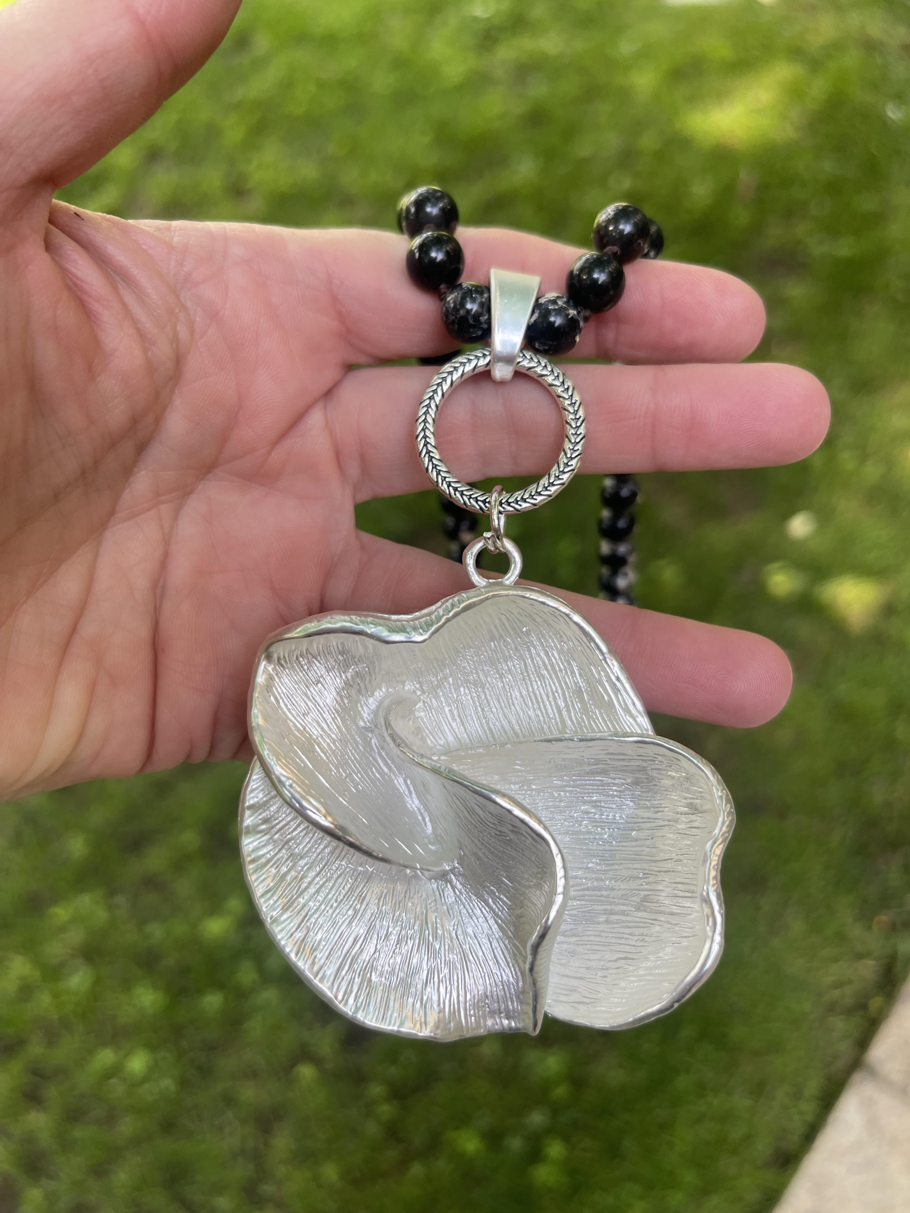 Collar Hippie Chic largo con precioso colgante de flor plateado opaco y piedras naturales anudadas negras con leves vetas blancas.